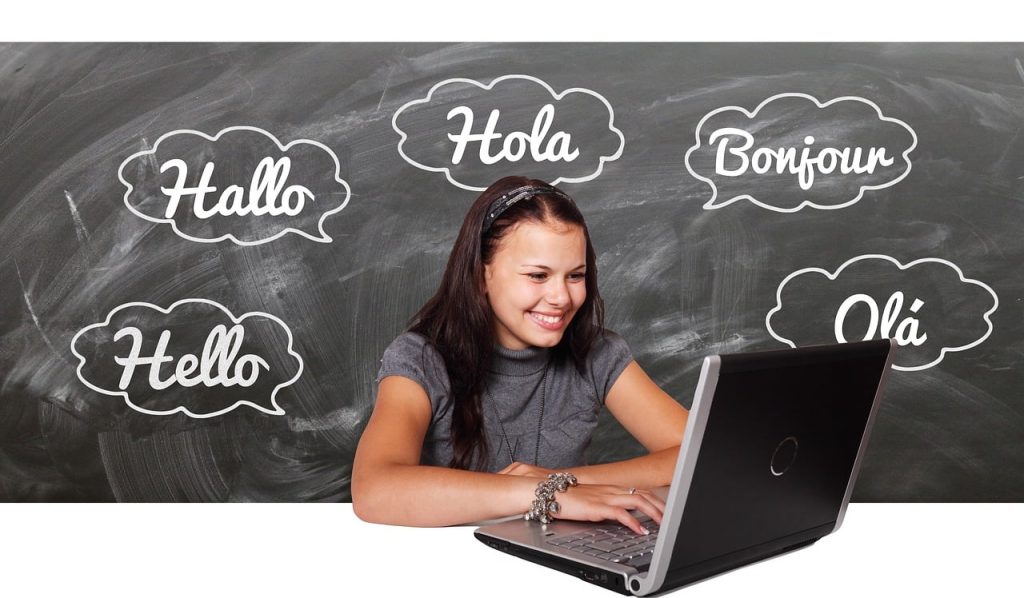 Mädchen am Laptop, Sprechblasen mit Hallo in verschiedenen Sprachen im Hintergrund